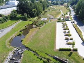 Luftaufnahme eines Wohnmobilstellplatzes am Rand einer Grünanlage. Ein Fluss windet sich durch die Wiesenflächen. Im Hintergrund bilden zwei Gewässerarme des Flusses eine Insel (Sonneninsel) mit einer befestigten Fläche und zwei Sitzbänken. Luftaufnahme eines Wohnmobilstellplatzes am Rand einer Grünanlage. Ein Fluss windet sich durch die Wiesenflächen. Im Hintergrund bilden zwei Gewässerarme des Flusses eine Insel (Sonneninsel) mit einer befestigten Fläche und zwei Sitzbänken.