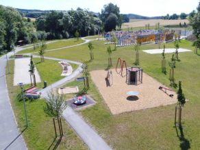 Luftaufnahme einer Grünanlage mit Kinderspielplatz, einem Geh- und Radweg und Wiesenflächen mit vereinzelten jungen Bäumen. Im Hintergrund ein Schilderpark (Fernweh-Park). Luftaufnahme einer Grünanlage mit Kinderspielplatz, einem Geh- und Radweg und Wiesenflächen mit vereinzelten jungen Bäumen. Im Hintergrund ein Schilderpark (Fernweh-Park).