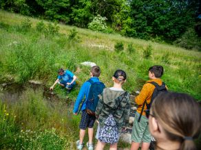 Ein Betreuer hockt an der renaturierten Selb und zeigt Kindern etwas am Bach bei einem Erlebnistag im Rahmen der Bayerisch-Tschechische Freundschaftswochen im Juni 2023. Ein Betreuer hockt an der renaturierten Selb und zeigt Kindern etwas am Bach bei einem Erlebnistag im Rahmen der Bayerisch-Tschechische Freundschaftswochen im Juni 2023.