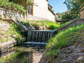 An einem kleinen Absturz im Stadtgebiet fällt das Wasser eines Bachs mit abgelöstem Strahl hinunter. An einem kleinen Absturz im Stadtgebiet fällt das Wasser eines Bachs mit abgelöstem Strahl hinunter.