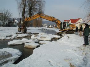 Ein Bagger arbeitet im Winter an einer rauen Rampe im Gewässerbett. Ein Bagger arbeitet im Winter an einer rauen Rampe im Gewässerbett.