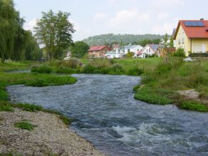 Eine dynamische Gewässerstrecke mit Kiesufer im Vordergrund und mäandrierendem Flussverlauf im Hintergrund. Angrenzend Wohnbebauung. Eine dynamische Gewässerstrecke mit Kiesufer im Vordergrund und mäandrierendem Flussverlauf im Hintergrund. Angrenzend Wohnbebauung.