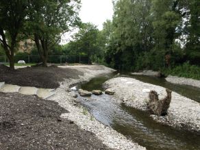 Ein neuer Erlebnisbereich mit Treppenstufen an das Wasser, einem verzweigten Gewässerverlauf, Trittsteinen über das Wasser und einer Kiesinsel mit Wurzelstock ist entstanden. Die Ufer und die Insel sind noch nicht begrünt. Ein neuer Erlebnisbereich mit Treppenstufen an das Wasser, einem verzweigten Gewässerverlauf, Trittsteinen über das Wasser und einer Kiesinsel mit Wurzelstock ist entstanden. Die Ufer und die Insel sind noch nicht begrünt.
