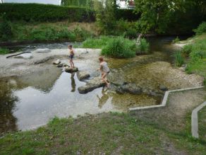 Zwei Kinder springen auf Trittsteinen über einen Gewässerarm der Würm. Der kiesige Bachlauf ist flach überströmt. Ein Treppenabgang führt an das Wasser. Die kleine, kiesige Insel im Hintergrund ist teilweise mit hohem Gras bewachsen. Zwei Kinder springen auf Trittsteinen über einen Gewässerarm der Würm. Der kiesige Bachlauf ist flach überströmt. Ein Treppenabgang führt an das Wasser. Die kleine, kiesige Insel im Hintergrund ist teilweise mit hohem Gras bewachsen.