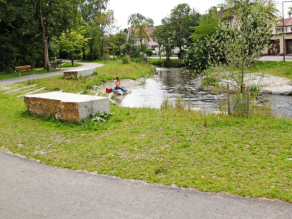 Erlebnisbereich an der Würm mit zwei großen Steinquadern am Ufer, einem Treppenabgang zum Wasser und einem asphaltierten Geh- und Radweg. Zwei Personen sitzen auf einem Felsen am Bach und hängen ihre Beine in das Wasser. Erlebnisbereich an der Würm mit zwei großen Steinquadern am Ufer, einem Treppenabgang zum Wasser und einem asphaltierten Geh- und Radweg. Zwei Personen sitzen auf einem Felsen am Bach und hängen ihre Beine in das Wasser.