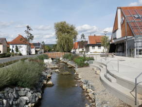 Ein Bach im städtischen Bereich mit Sitzstufen am Ufer und einer Kneippanlage im Gewässer. Ein Bach im städtischen Bereich mit Sitzstufen am Ufer und einer Kneippanlage im Gewässer.