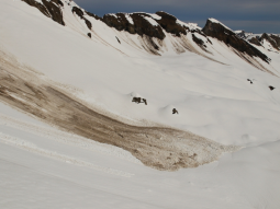 Große braune (mitgerissenens Untergrundmaterial) Nassschneelawinenablagerung in der hochalpinen, weißen Winterlandschaft.