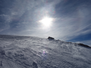 Schneefegen auf einer glänzenden, verharschten Schneeoberfläche. Die Sonne scheint durch einen Schleier aus Zirruswolken