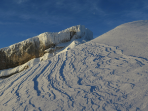 Wind hat den Schnee im Vordergrund stark bearbeitet. Im Hintergrund ist der Ifen mit Anraum vor wolkenlosem Himmel zu sehen.