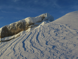 Wind hat den Schnee im Vordergrund stark bearbeitet. Im Hintergrund ist der Ifen mit Anraum vor wolkenlosem Himmel zu sehen.