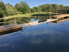 Teich mit einem durch Holzstege begehbaren Einbau aus Beton mit der Möglichkeit durch eine Scheibe unter das Wasser zu schauen.
