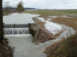 Ein Wehr mit aufgestautem Teich und Umgehungsgerinne. Aufgrund eines Hochwassers ist der Teich vollgefüllt und fließt über das Wehr und das Umgehungsgerinne aus.