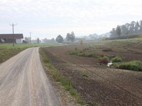 Mäandrierender Bach mit erstem Uferbewuchs, daneben fertig gestaltete, noch unbewachsene Flächen. Links verläuft der neue Fuß- und Radweg.