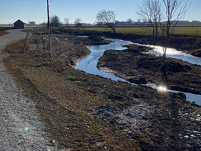 Renaturierter Bach mit Insel und neuen Gehölzanpflanzungen. Randlich ein wassergebundener Weg und ein Stadel.