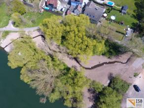 Luftaufnahme eines neu angelegten, geschwungenen Bachlaufs mit Störsteinen u. a. im Gewässer. Daneben schließt Wald an und auf einer Seite ein Fluss, auf der anderen Wohnbebauung.