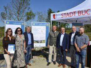 Die Preisträger und MD Dr. Detsch stehen links und rechts neben dem Preisträgerplakat. Eine Person hält eine Urkunde in der Hand.