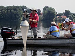 Personen auf einem Boot, die eine Wasserprobe über ein Netz mit Kegelaufsatz filtrieren