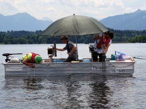 Boot auf einem See mit drei Personen, die Wasserproben nehmen.
