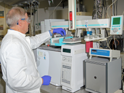 Ein Labormitarbeiter mit Schutzbrille und Handschuhen befüllt den Gaschromatograph mit Probenfläschchen.