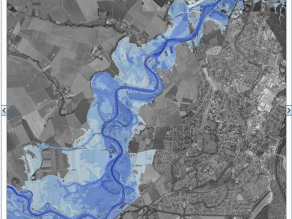 Kartenausschnitt eines Gewässers.Entlang des abgebildeten Flusses breiten sich an beiden Seiten in blau dargestellte Überschwemmungsgebiete aus. Unterschiedliche Blautöne der Flächen verdeutlichen verschiedene Wassertiefen im Hochwasserfall.