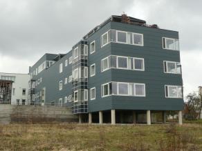 Wohnhaus steht auf Betonsäulen in einem Bereich, der von Hochwasser durchflossen werden kann. Dahinter ist die Hochwasserschutzmauer aus Beton.