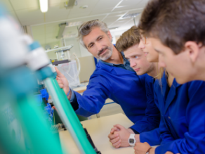 Drei Auszubildenden wird eine technische Einrichtung durch einen Lehrer erläutert. Drei Auszubildenden wird eine technische Einrichtung durch einen Lehrer erläutert.