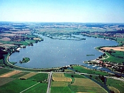 Der Altmühlsee liegt inmitten des Altmühltals und ist vollständig von einem Damm umgeben. Auf dem Luftbild erkennt man am hinteren Rand des Sees die Flachwasser- und Inselzone zum Schutz gefährdeter Pflanzen- und Tierarten.