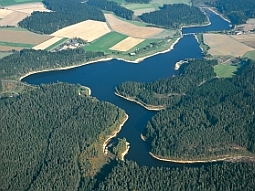 Das Luftbild zeigt den zu dreiviertel im mit Wald umgebenen Liebensteinspeicher. Im oberen rechten Teil des Bildes überquert eine Brücke den Stausee. Das Absperrbauwerk selbst befindet sich am linken Bildrand.