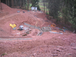 Schurf im Berghang mit freigelegtem, verwittertem Buntsandstein, wo bereits die Herdmauer aus Beton und der Quellschacht errichtet wurden.