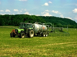 Mit einem Traktor mit Saugwagen wird Gülle auf einer Wiese verteilt.