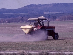 Mit einem Traktor wird Dünger mit einem Streugerät auf einem Feld ausgebracht.
