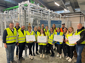 Gruppenbild vor dem Elektrolyseur der Energieerzeugung Wunsiedel, alle mit Warnwesten und einigen Schildern der Wasserstoffkampagne in der Hand