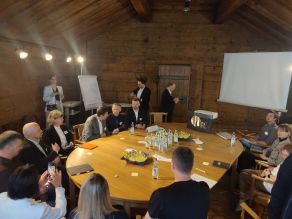 Teilnehmer einer der Arbeitsgruppen in einem Raum des Haus der Begegnung, in Diskussion am Tische sitzend bzw. einige stehend.