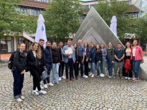 Gruppenfoto, Teilnehmer der Sommerakademie mit der Betreuerin und einem Referenten vor dem Kunstobjekt an der Hochschule für den öffentlichen Dienst in Bayern, Fachbereich Allgemeine innere Verwaltung.