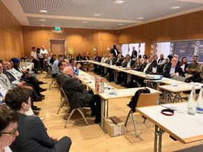 Teilnehmer des in einem Vortragsraum des Kongresszentrums der Messe München organisierten Workshops; auf Stühlen sitzend, bzw. an in U-Form angeordneten Tischen im Zentrum des Raums die Richtung Bühne blicken.