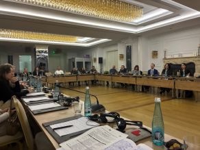 Viele Personen sitzen an Tischen in U-Form.